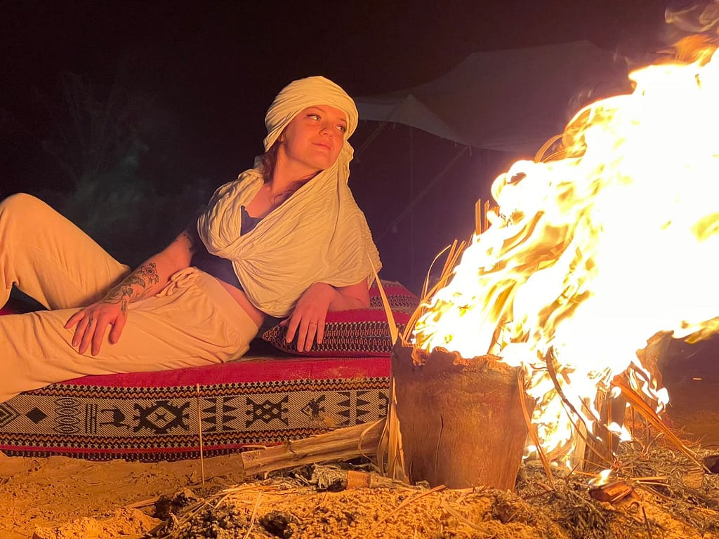 A group of people sitting around a campfire in the desert under a starry sky.