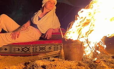 A group of people sitting around a campfire in the desert under a starry sky.