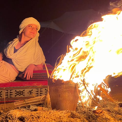 A group of people sitting around a campfire in the desert under a starry sky.