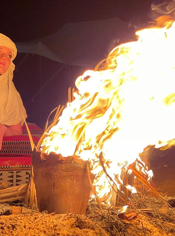 A group of people sitting around a campfire in the desert under a starry sky.