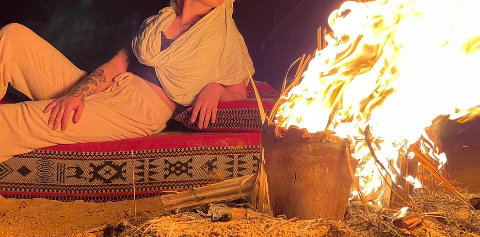 A group of people sitting around a campfire in the desert under a starry sky.